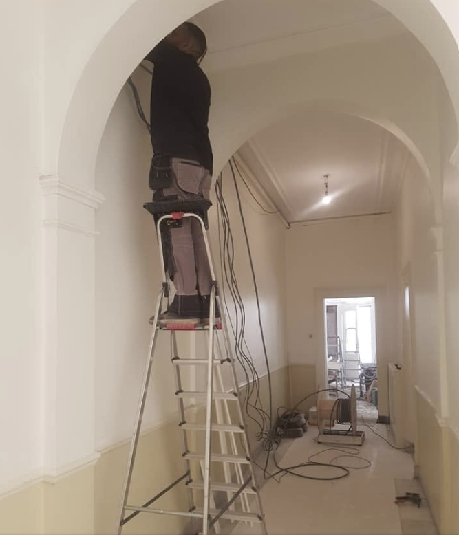 Elektricien Fred v Leeuwen werkt op een ladder aan de elektrische bedrading in een hal